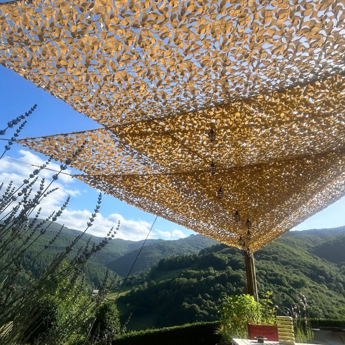 Filets de camouflage triangulaires beiges sur une terrasse avec vue sur la montagne