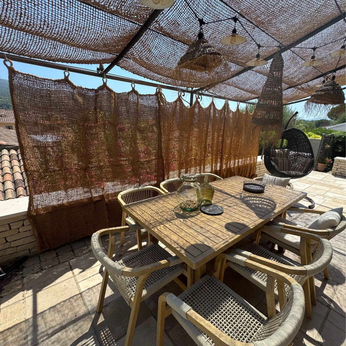 Rideau en fibre de coco suspendu sur une terrasse avec table à manger